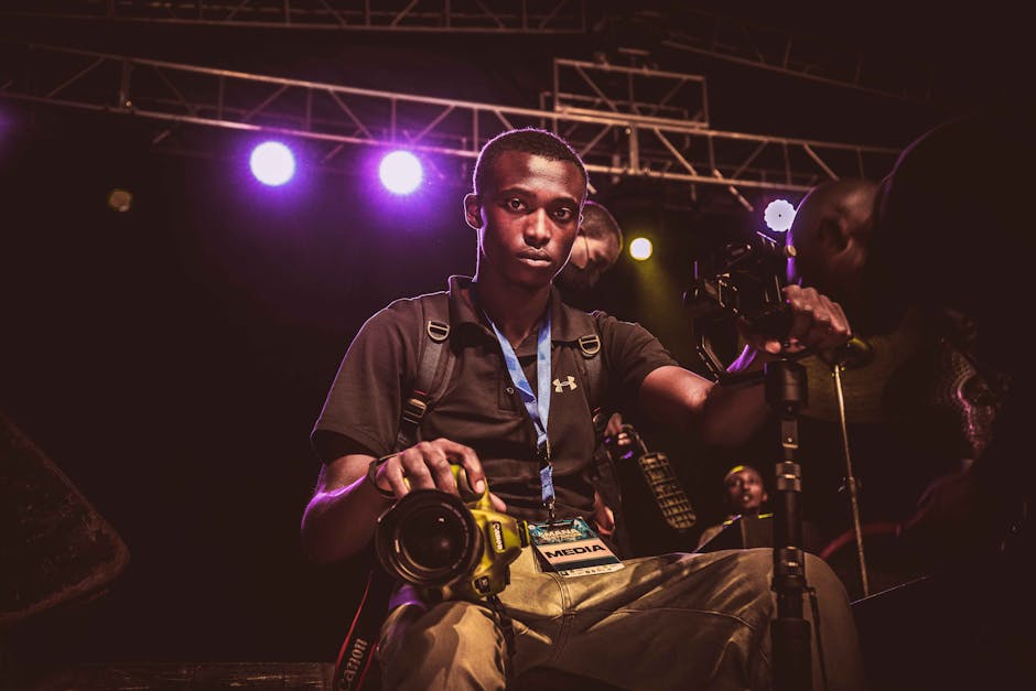 Portrait of a photographer with camera and monopod on a dimly lit stage.